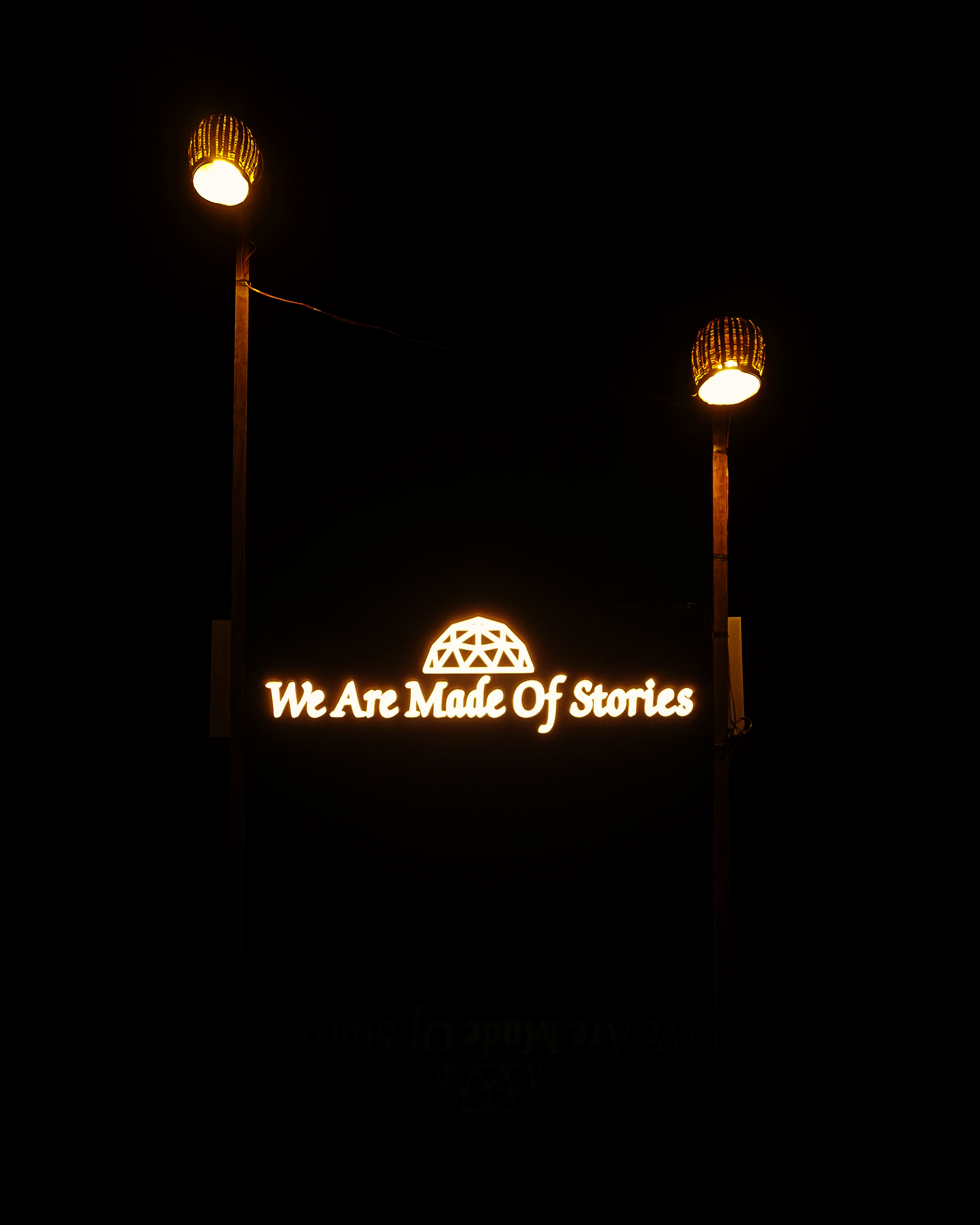 Illuminated We Are Made Of Stories sign with dome logo, lit up at the property entrance at night