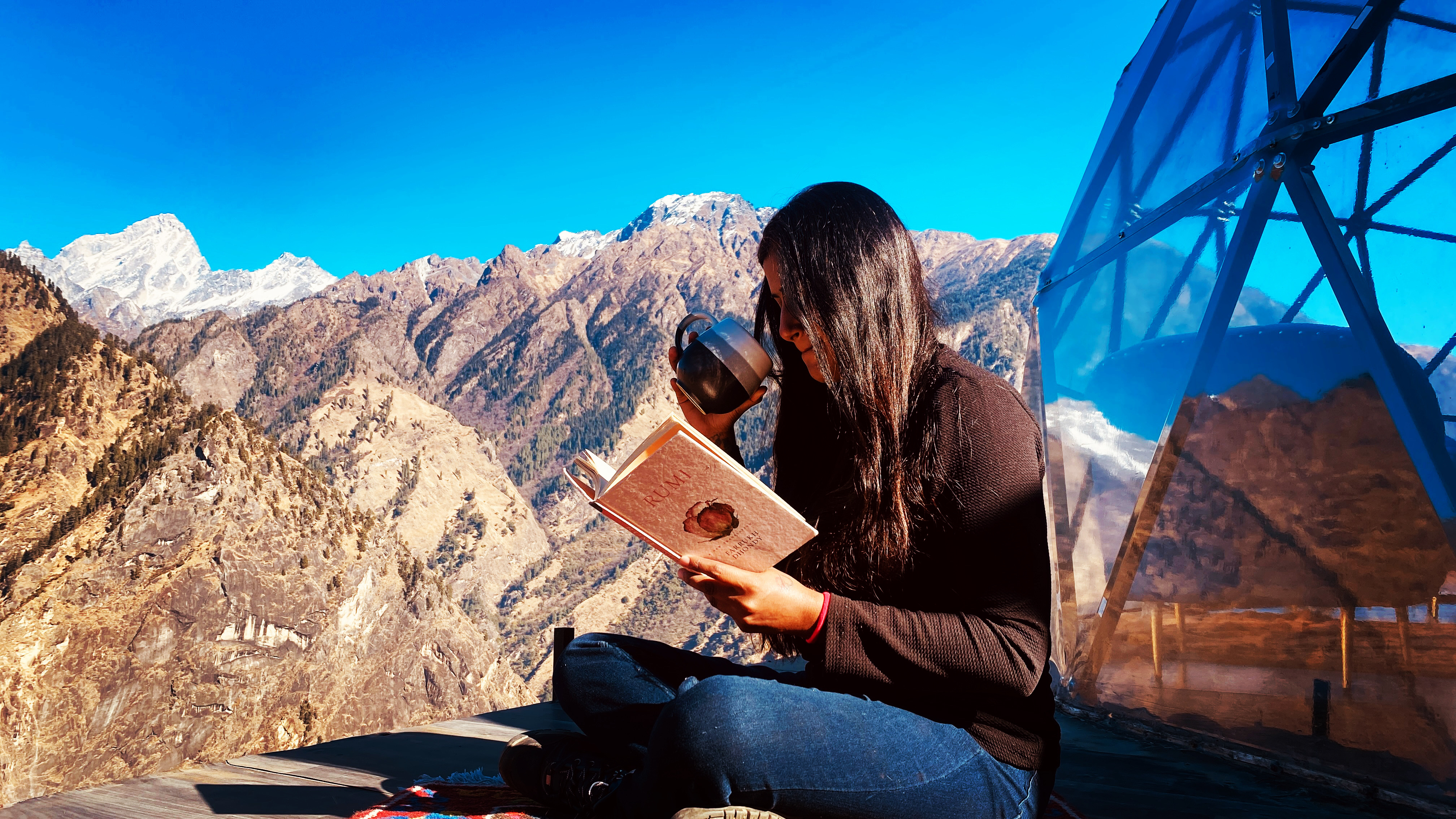 Guest reading by lamplight inside a glass dome with coffee, Himalayan peaks visible outside