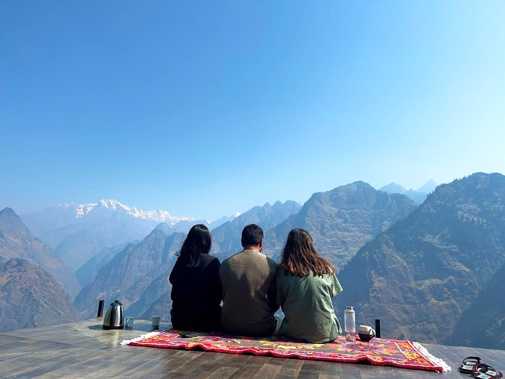 Guests sitting together on a rug at the cliff edge, taking in the Himalayan valley view