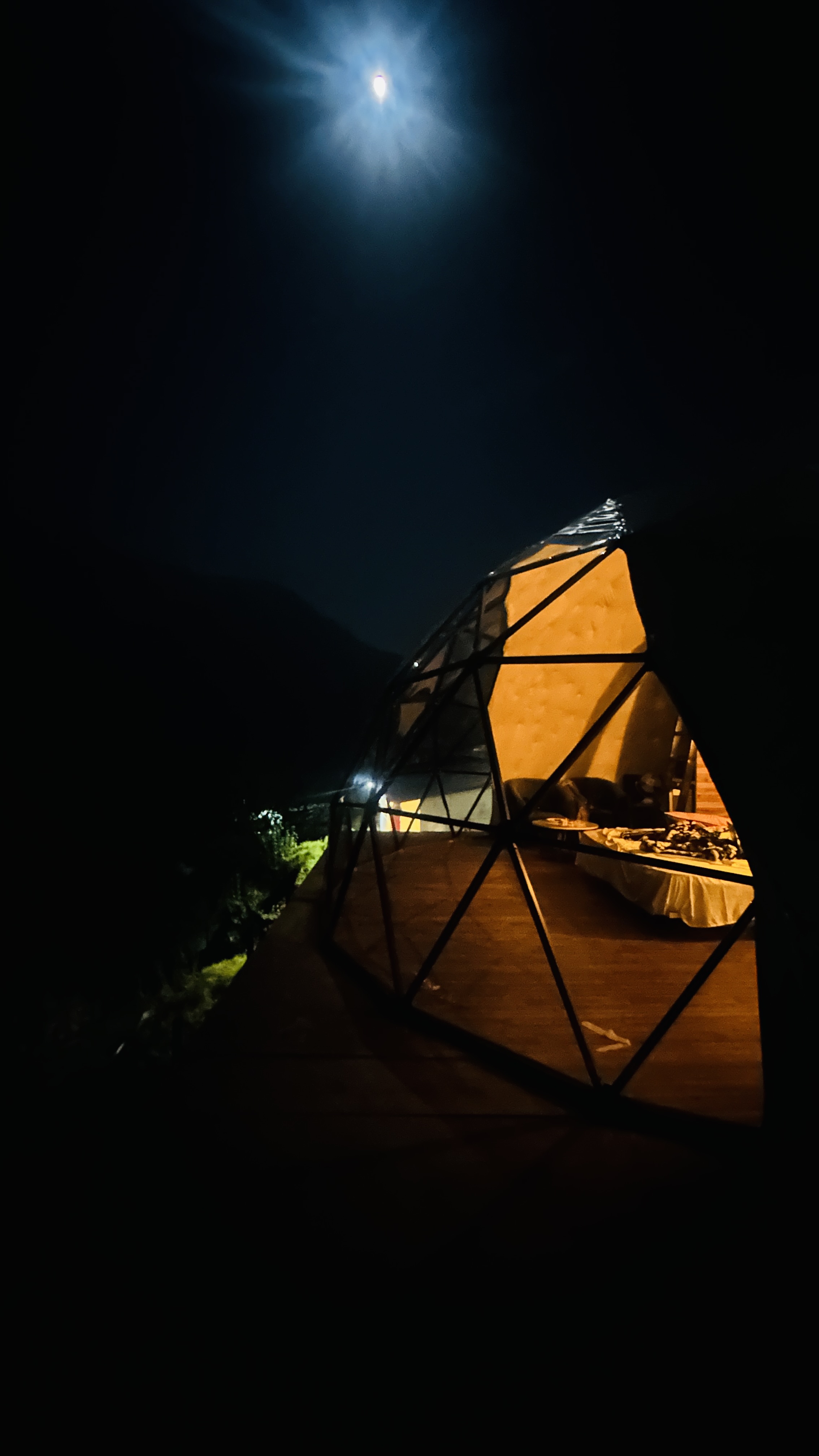 Geodesic dome interior lit warmly at night with the moon overhead
