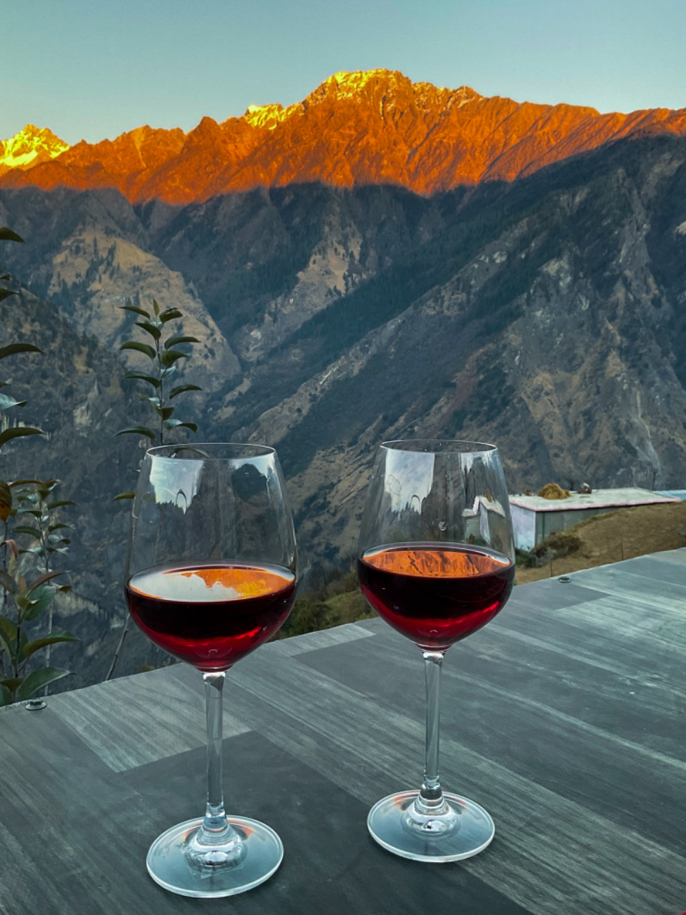 Two glasses of wine on a terrace table at sunset with alpenglow on the peaks